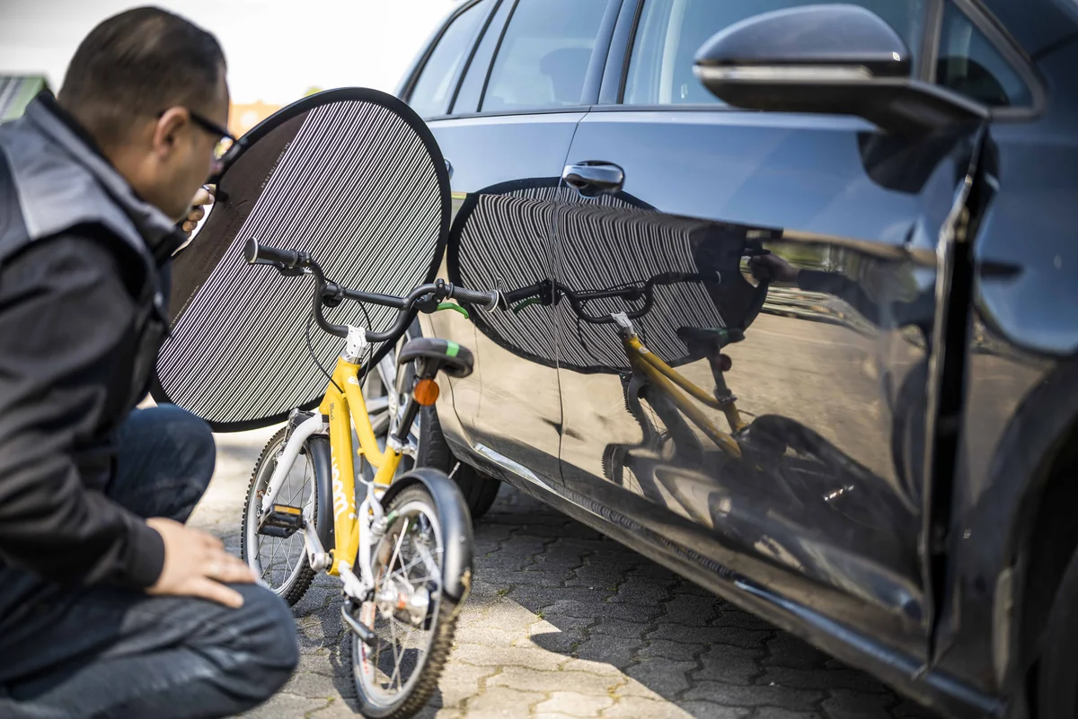 Sachverständiger prüft einen Fahrzeugschaden neben einem Kinderfahrrad.