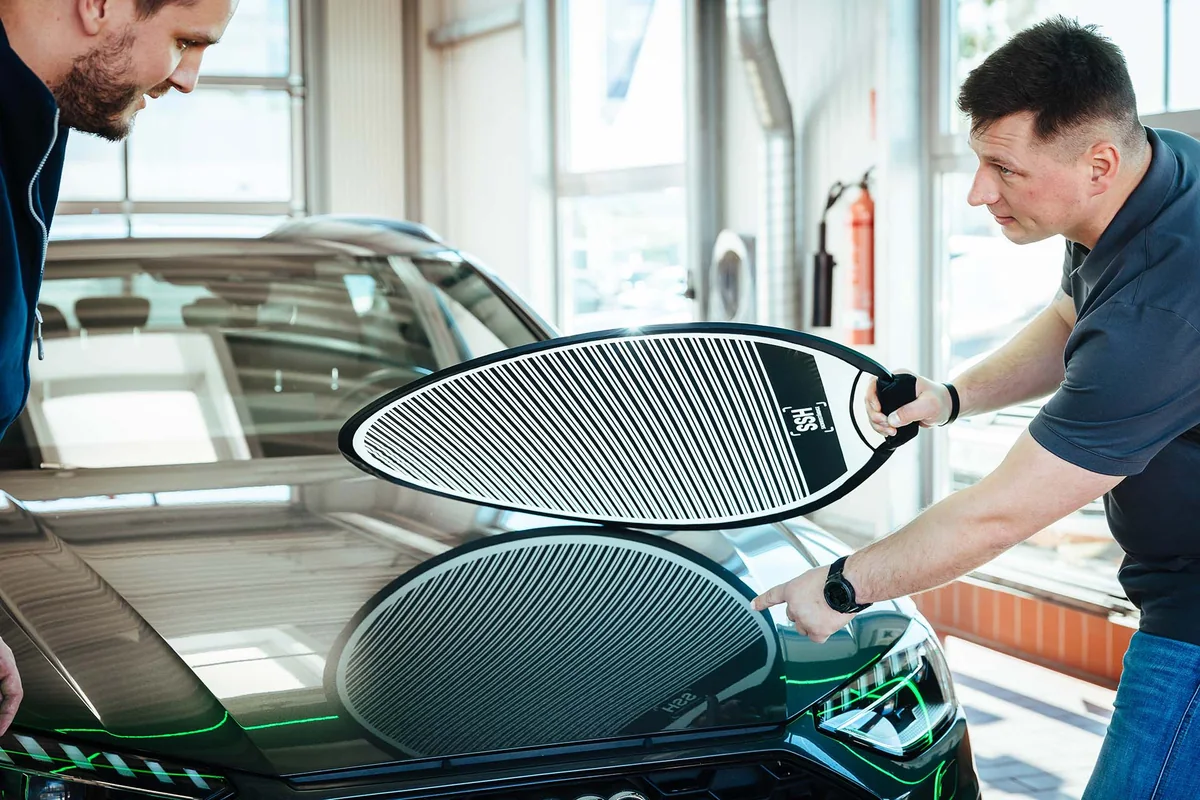Zwei Männer prüfen die Motorhaube eines Autos mit einem Dellensegel.