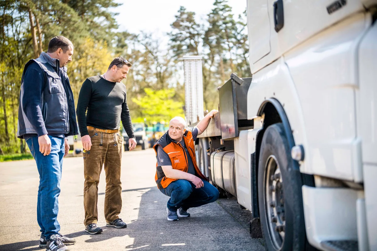 Sachverständige besichtigen gemeinsam mit einem Fahrer einen Lastwagen.